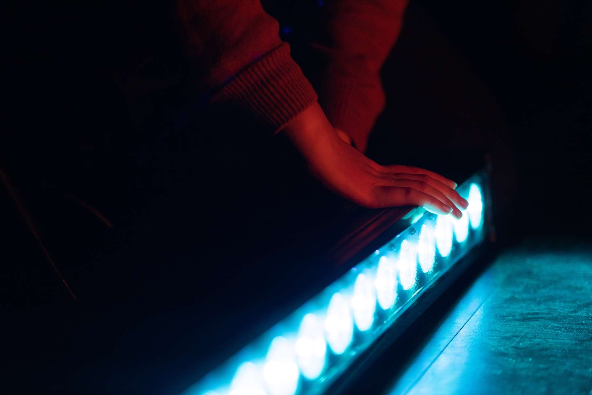 Photos d'une lumière bleue en longueur, posée sur la scène de La Pokop. Deux mains sont posées sur la lumière pour l'installer.
